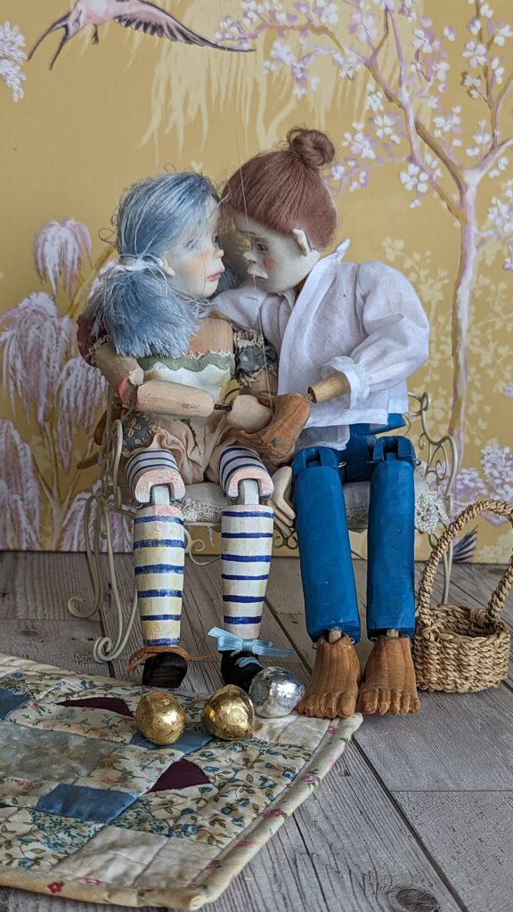 2 wooden art dolls sitting together 